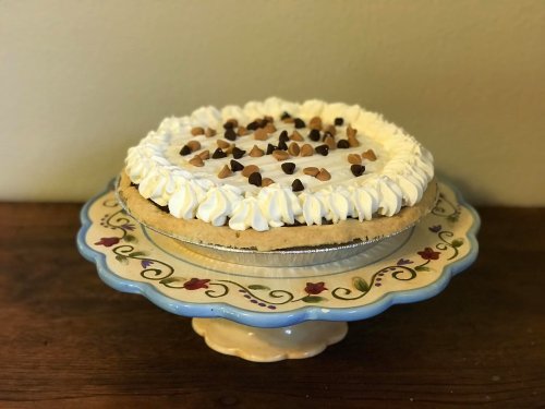 A creamy pie topped with whipped cream and chocolate chips, displayed on a decorative cake stand.