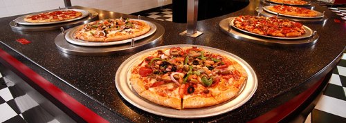 A variety of pizzas on display at a buffet, featuring different toppings on metal trays.