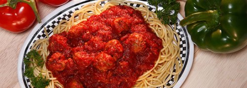 A plate of spaghetti topped with meatballs and marinara sauce, garnished with parsley, alongside red and green peppers.