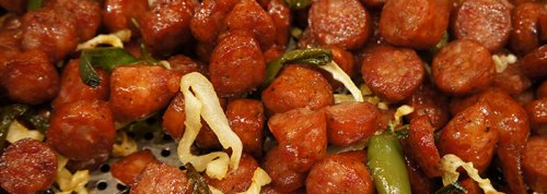 Close-up of cooked sausage pieces mixed with green peppers and cabbage, glistening with seasoning.