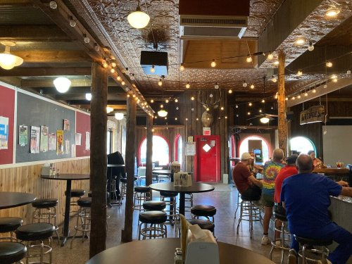 Interior of a casual bar with wooden beams, string lights, and patrons sitting at tables and the bar.