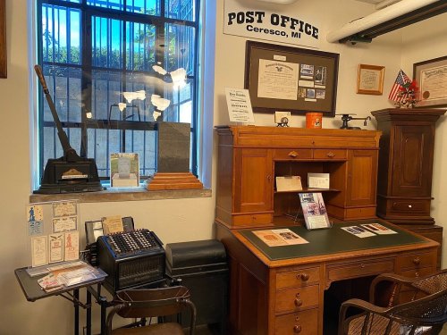 A vintage post office interior featuring a wooden desk, old-fashioned equipment, and historical memorabilia on the walls.