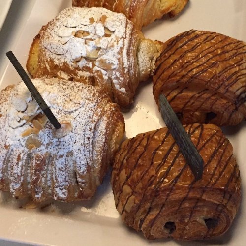 Two pastries on a plate: one is almond croissant dusted with powdered sugar, the other is a chocolate-drizzled croissant.
