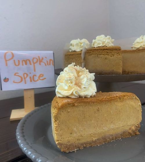A slice of pumpkin spice cheesecake topped with whipped cream, next to a sign that reads "Pumpkin Spice."