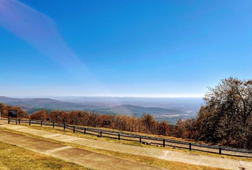 A panoramic view of rolling hills and valleys under a clear blue sky, with a paved path in the foreground.