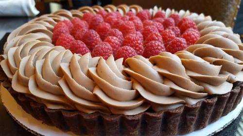 A chocolate tart topped with swirls of cream and fresh raspberries arranged in a circular pattern.