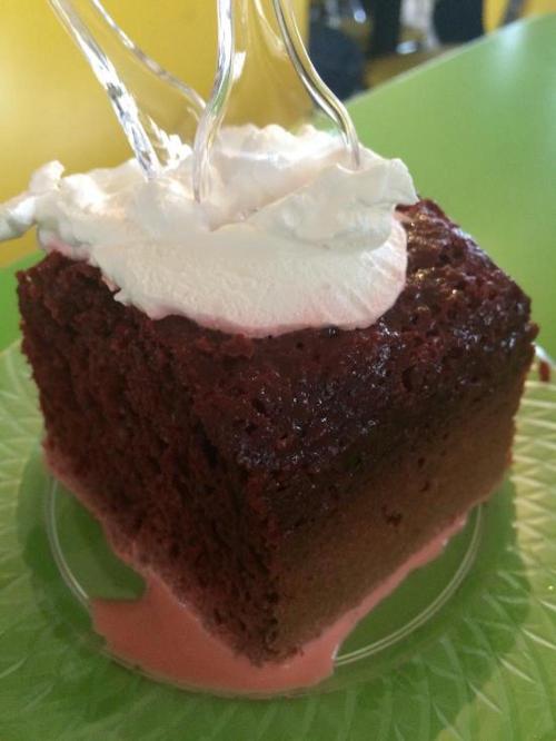 A slice of red velvet cake topped with whipped cream on a green plate, with a pink sauce underneath.