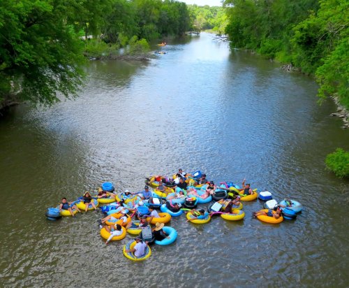 A group of people floating on colorful inner tubes in a river, surrounded by lush greenery and calm water.