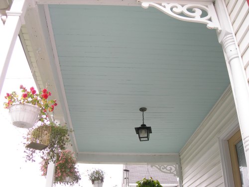 A porch ceiling painted light blue, featuring decorative white trim and hanging flower baskets.