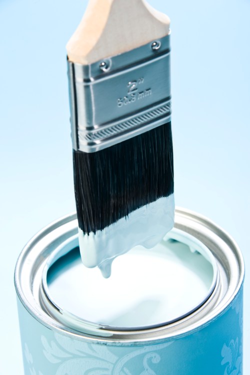 A paintbrush dripping with light blue paint above an open paint can against a soft blue background.