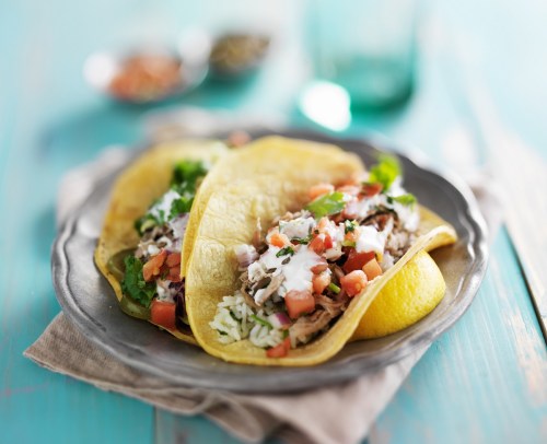 Two tacos filled with shredded meat, lettuce, tomatoes, and topped with sour cream, served on a silver plate.