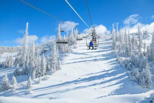 A ski lift ascends a snowy mountain, surrounded by frosted trees under a clear blue sky.