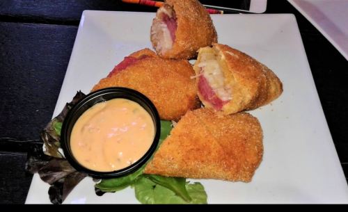 Crispy fried rolls filled with meat and cheese, served with a dipping sauce on a white plate with greens.