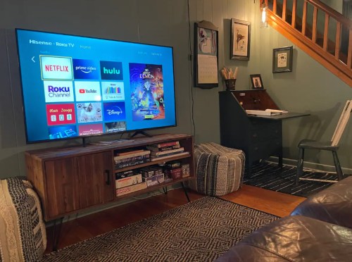 Cozy living room with a TV displaying streaming apps, a wooden cabinet, and a desk in a warm, inviting space.