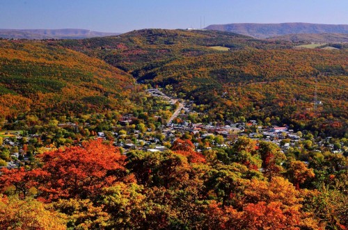 A scenic view of a valley town surrounded by vibrant autumn foliage and rolling hills under a clear blue sky.