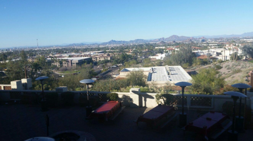 A panoramic view of a cityscape with mountains in the background, featuring buildings and outdoor seating areas.