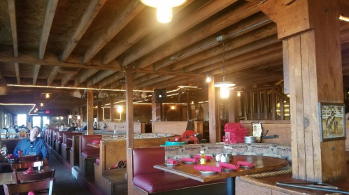 Interior of a rustic restaurant featuring wooden beams, red booths, and tables set for dining.