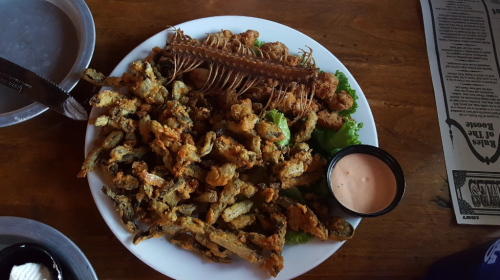A plate of fried seafood, including shrimp, soft-shell crab, and fried vegetables, served with a dipping sauce.