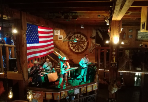A lively band performs on stage in a rustic venue adorned with an American flag and Western decor.