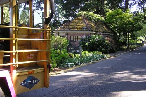 A view of a garden entrance with a bus in the foreground, surrounded by lush greenery and flowers.