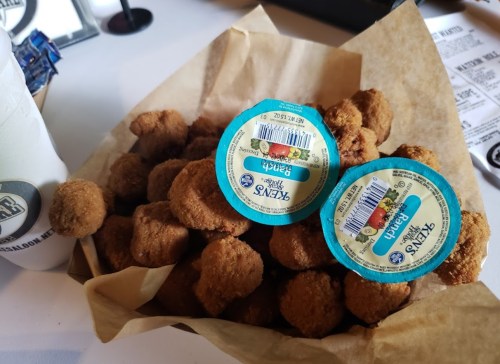 A basket of golden-brown chicken nuggets with two dipping sauce containers on top.