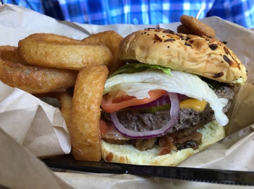 A juicy burger with lettuce, tomato, onion, and cheese, served with crispy onion rings on the side.