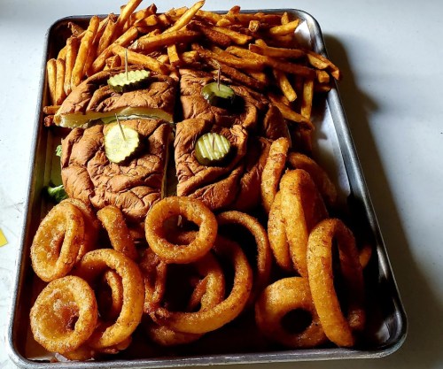 A large tray featuring a sandwich with pickles, surrounded by golden fries and onion rings.
