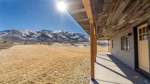A sunny view from a porch overlooking a grassy field and snow-capped mountains in the background.