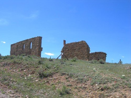 Ruins of a stone building on a grassy hillside under a clear blue sky.