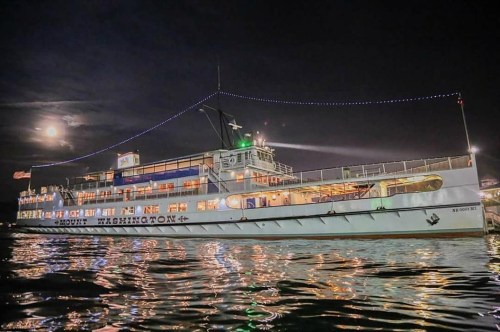 A lit-up boat named "Mount Washington" on calm waters at night, with a full moon in the background.