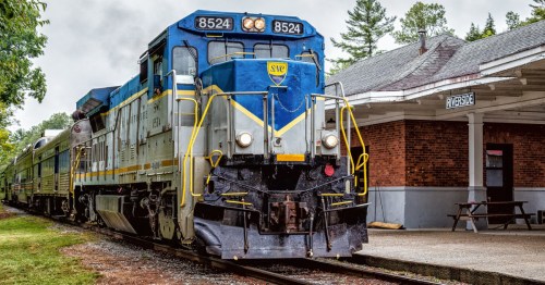 a blue and silver train with the Saratoga & North Creek Railway, New York pulls into the riverside station