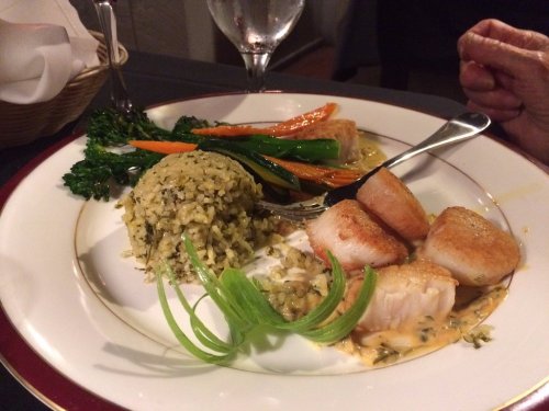 A plate featuring seared scallops, herbed rice, sautéed vegetables, and a garnish of green onion.