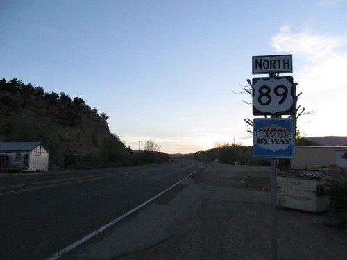 Sign for North 89 Scenic Byway along a quiet road, with a sunset in the background and mountains nearby.