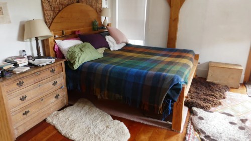 Cozy bedroom with a wooden bed, colorful blankets, a nightstand, and soft rugs on a wooden floor.