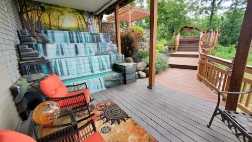 A cozy outdoor space featuring a mural of a waterfall, colorful cushions, and a wooden deck with a garden view.