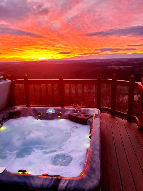 A hot tub on a deck with a stunning sunset and colorful sky in the background.