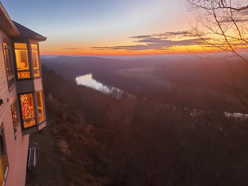 A scenic sunset view over a river, with a house decorated for the holidays in the foreground.