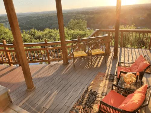 A scenic balcony with wooden railings, two chairs, and a view of rolling hills at sunset.