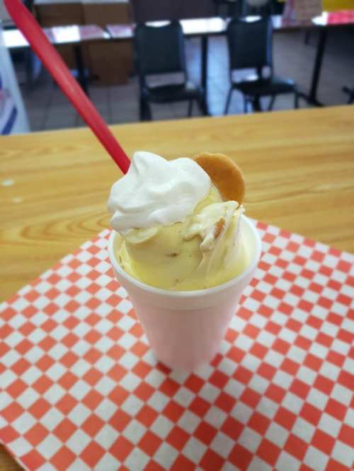 A cup of creamy ice cream topped with whipped cream and a cookie, placed on a checkered tablecloth.