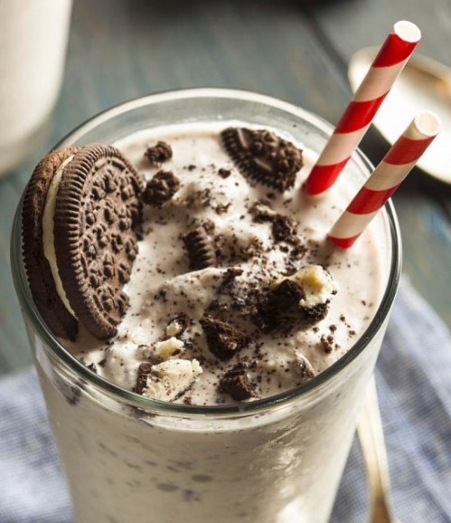 A creamy milkshake topped with crushed cookies and two red and white striped straws.