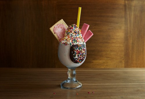 A colorful milkshake topped with whipped cream, sprinkles, a chocolate-dipped treat, and wafer cookies in a glass.
