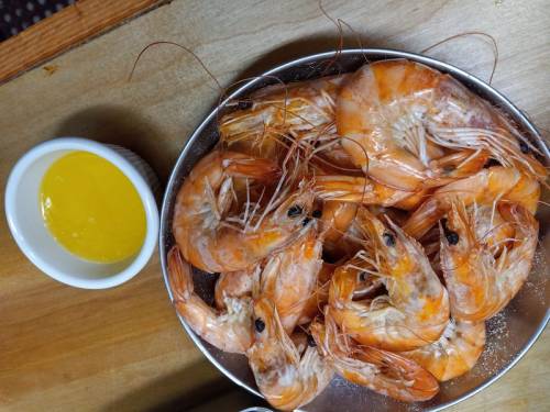 A silver plate filled with cooked shrimp next to a small bowl of yellow dipping sauce.