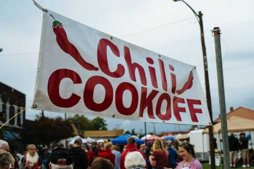 A banner reading "Chili Cookoff" hangs above a bustling outdoor event with people and tents in the background.