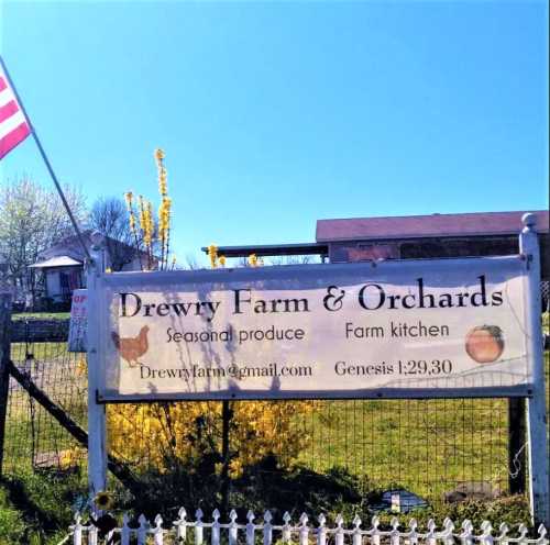 Sign for Drewry Farm & Orchards featuring seasonal produce, a farm kitchen, and a biblical reference. American flag in background.