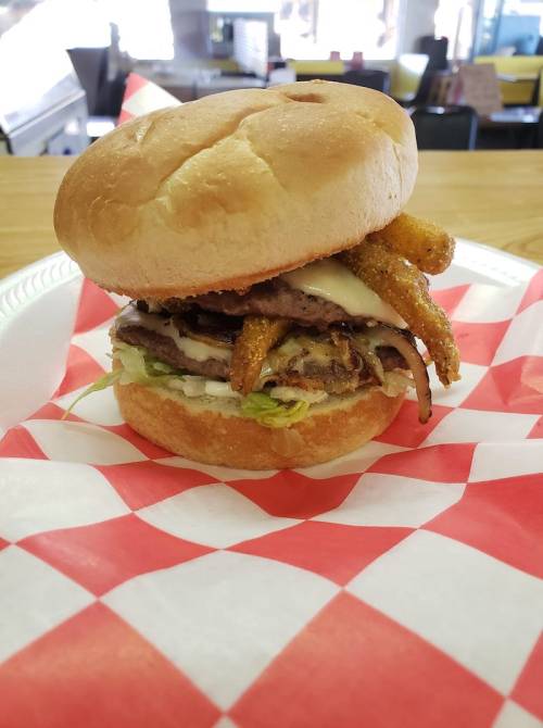 A stacked burger with lettuce, mayonnaise, and crispy onion rings on a toasted bun, served on a red and white checkered plate.