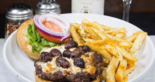 A plate featuring a burger with olives, lettuce, tomato, and onion, served with a side of seasoned fries.