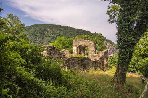 Ruins of a stone structure surrounded by lush greenery and hills under a partly cloudy sky.