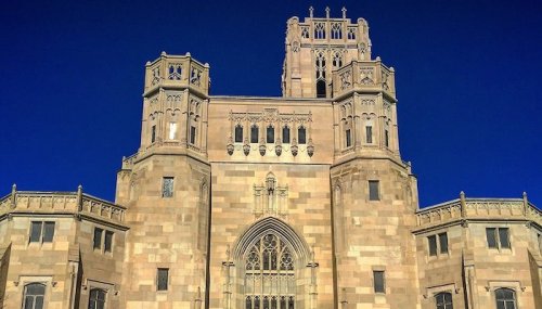 A grand stone building with intricate architectural details and tall towers against a clear blue sky.