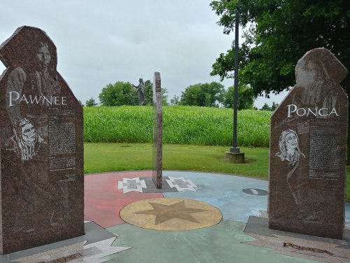 Two granite monuments labeled "Pawnee" and "Ponca" stand in a grassy area, with a statue visible in the background.