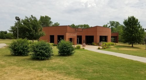 A modern brick building surrounded by greenery and trees, with a paved path leading to it.